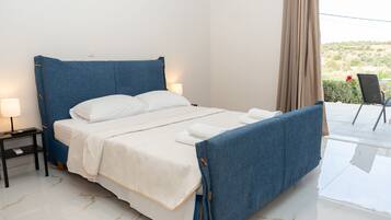 Una cama bien hecha con cabecera azul, ropa de cama blanca y una mesita de noche con lámpara.