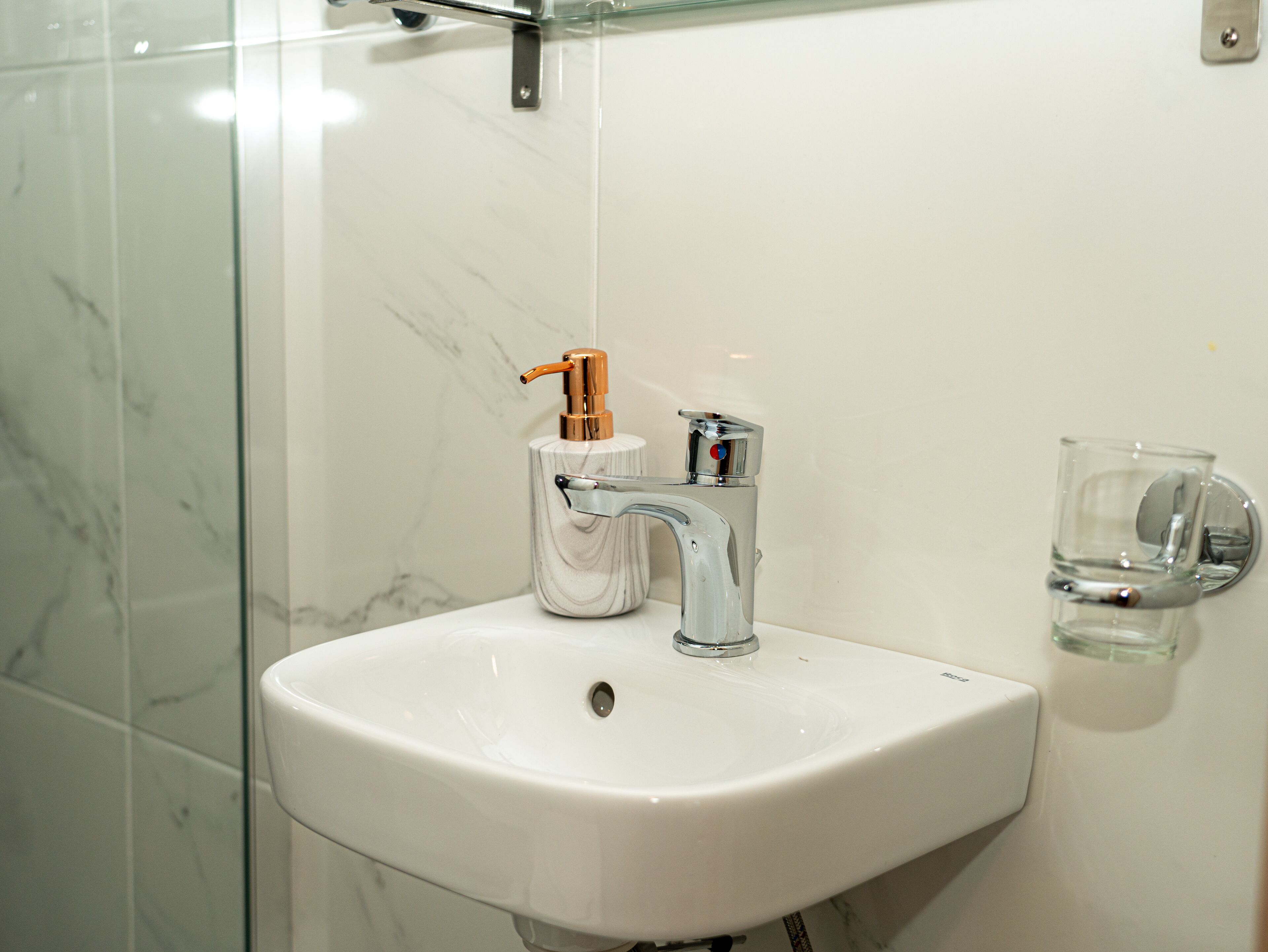 Un baño con un lavamanos blanco, un grifo de cromo y un dispensador de jabón.