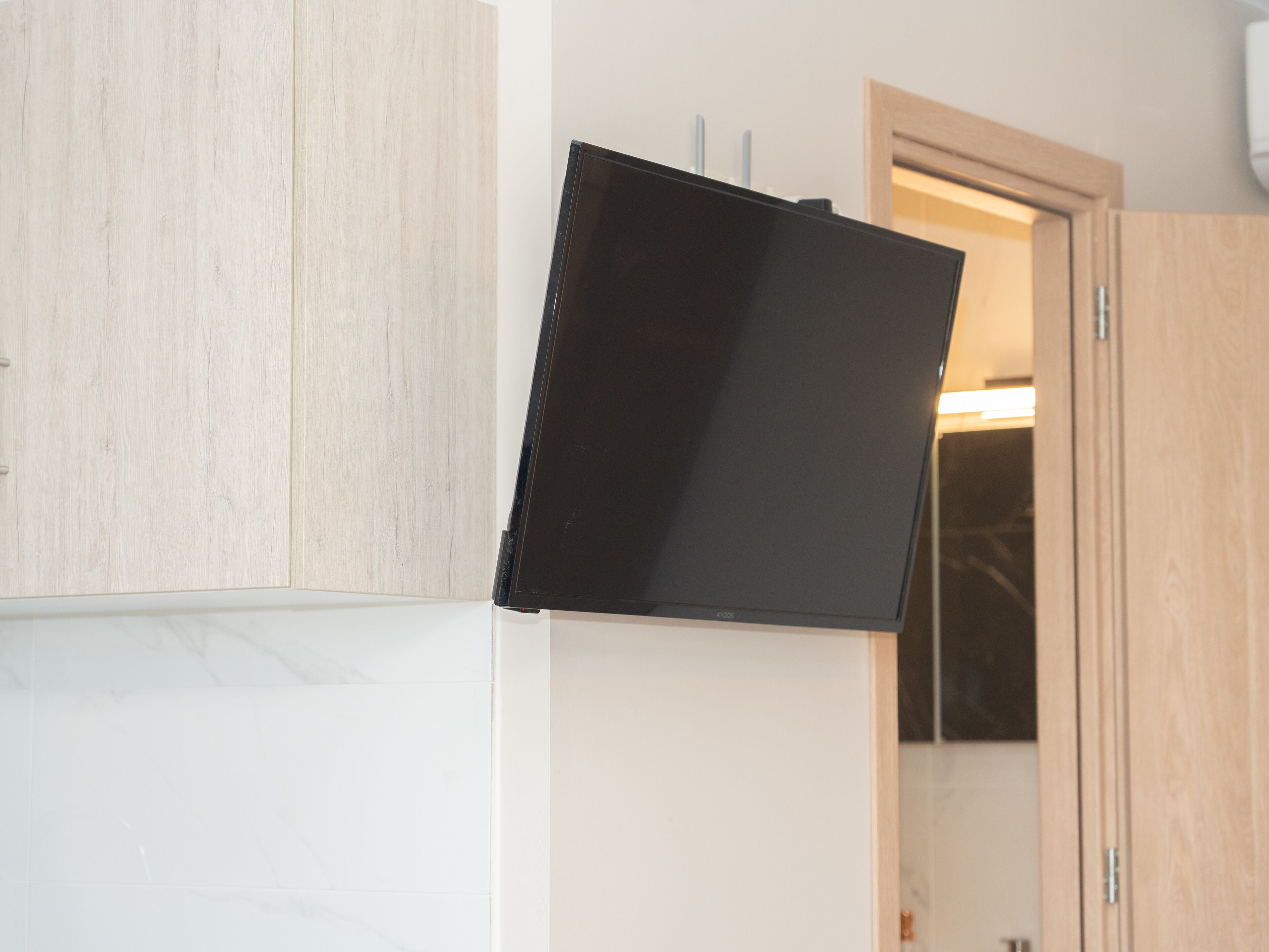 Una habitación con televisión de pantalla plana montada en la pared, muebles de madera y una puerta que da a otra estancia.