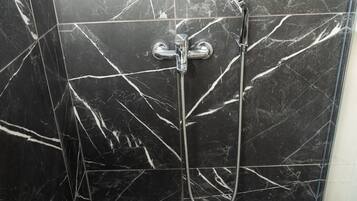 A bathroom with black marble tiles and a shower with a handheld showerhead.