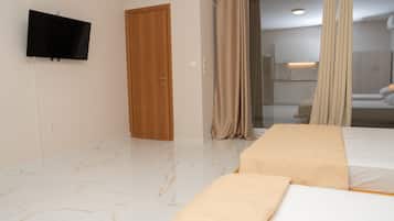 A modern hotel room with a flat-screen TV mounted on the wall, a wooden door, a sliding glass door leading to a bathroom, and two beds with beige bedding.