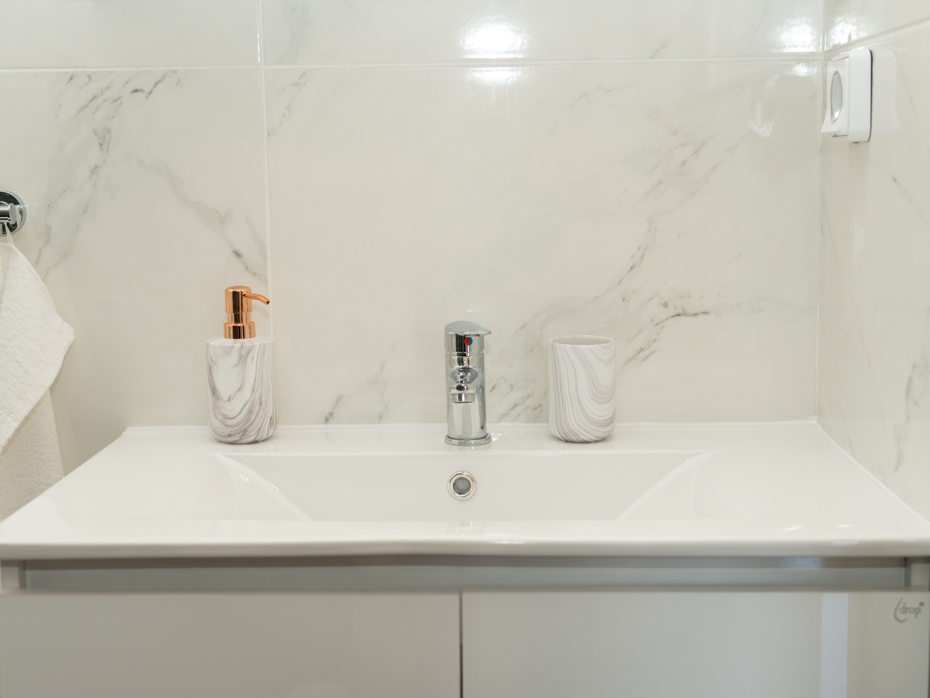 Un baño con lavamanos de mármol blanco, un grifo moderno y una taza de mármol.