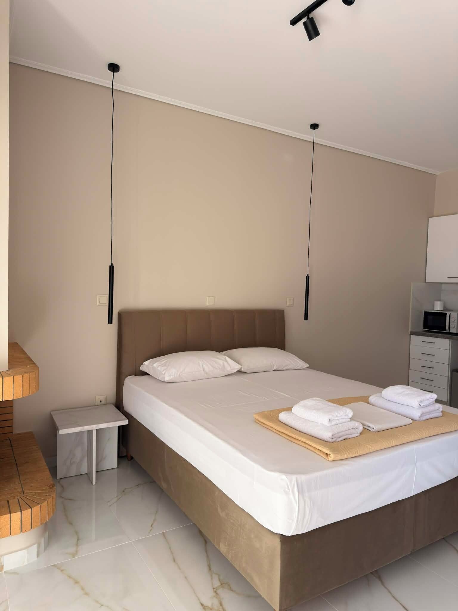 A modern hotel room with a large bed, bedside tables, a small bedside table, a flat-screen TV, and a microwave.