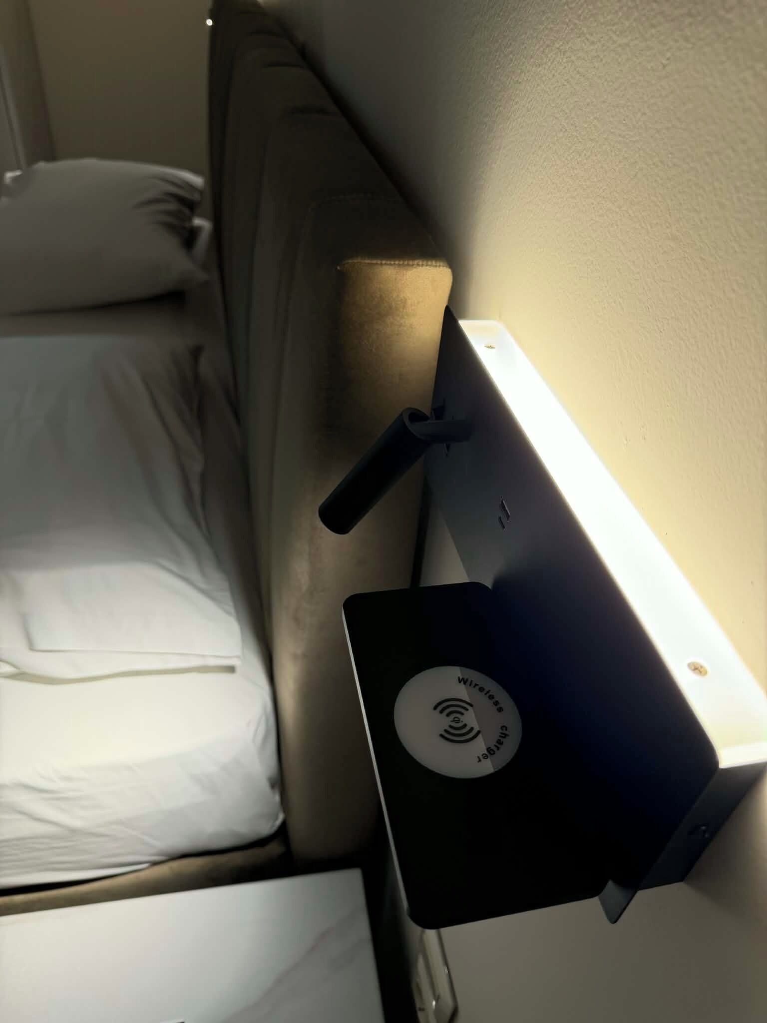A bed with a headboard, a bedside table with a wireless charger, and a wall-mounted light fixture.