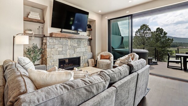 A modern living room with a stone fireplace, a large flat-screen TV, and a comfortable sectional sofa. - New Luxury w/ AC | Close to Slopes | Hot Tub | Valley View Villa 11 (Angel Fire)