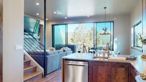 A modern kitchen with a dishwasher, a dining area with a table and chairs, and a staircase leading to an upper level. - New Luxury w/ AC | Close to Slopes | Hot Tub | Valley View Villa 11 (Angel Fire)
