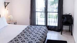 A bedroom with a bed, a chair, a table with a lamp, and a window with curtains. - Best Located Executive Apartment in Maroussi
 (Marousi)