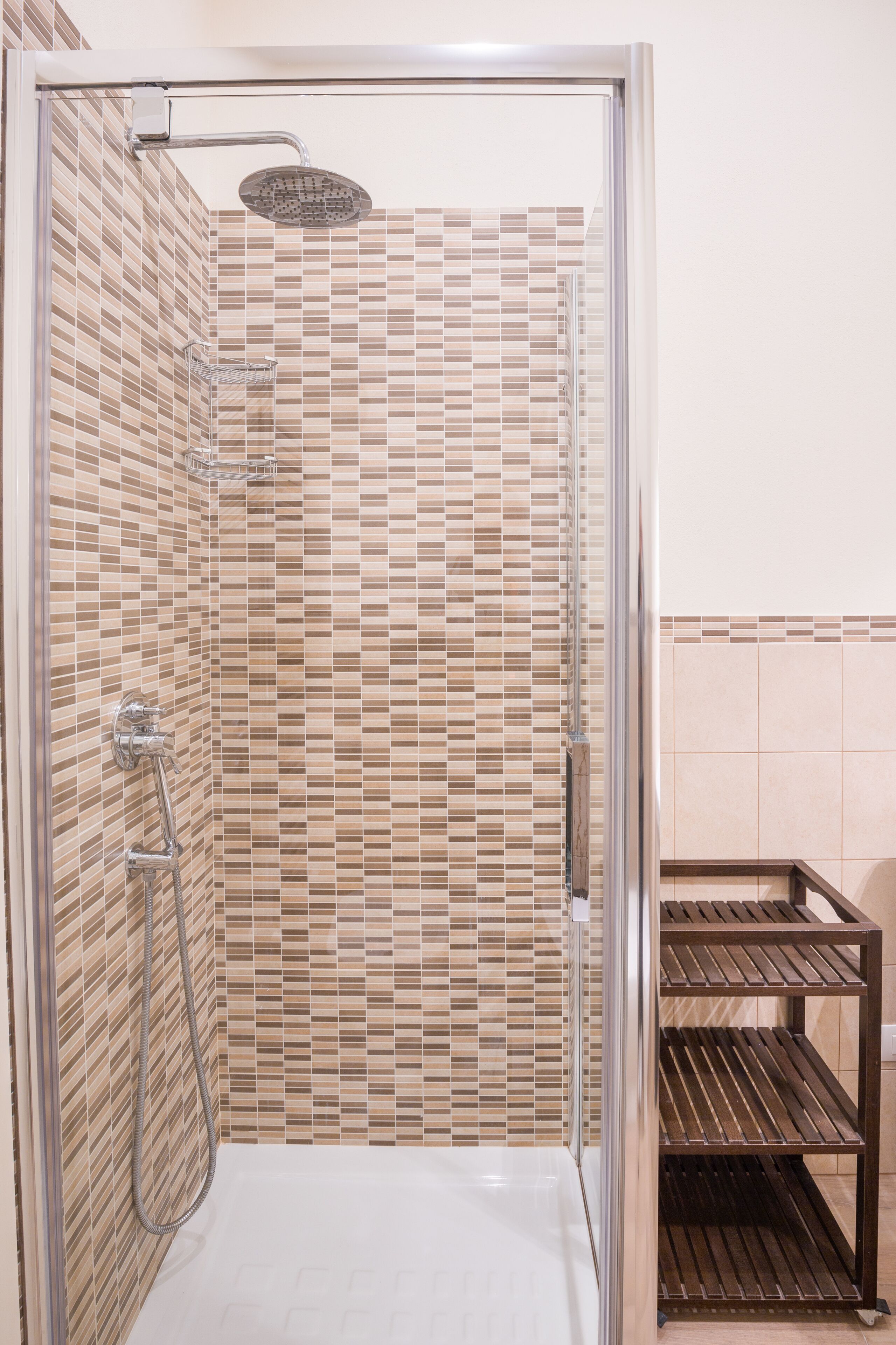 A shower with a glass door, tiled walls, and a metal shelf unit beside it.