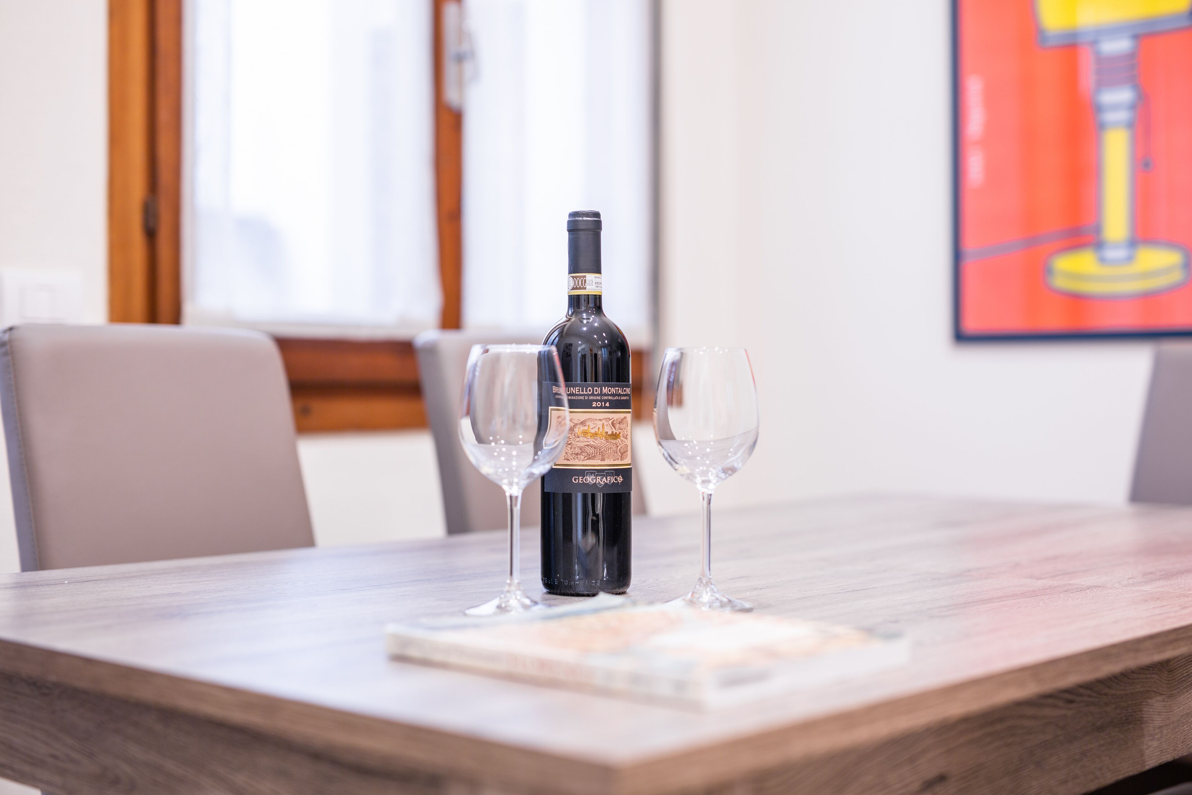 A bottle of Brunello di Montalcino wine on a table with two empty wine glasses.