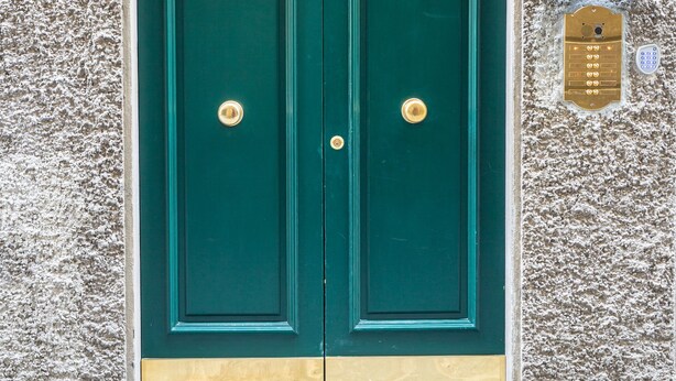 Une porte à deux battants, dotée d’un clavier pour le verrouillage, encastrée dans un mur à texture, et une plaque d’immatriculation indiquant l’adresse.