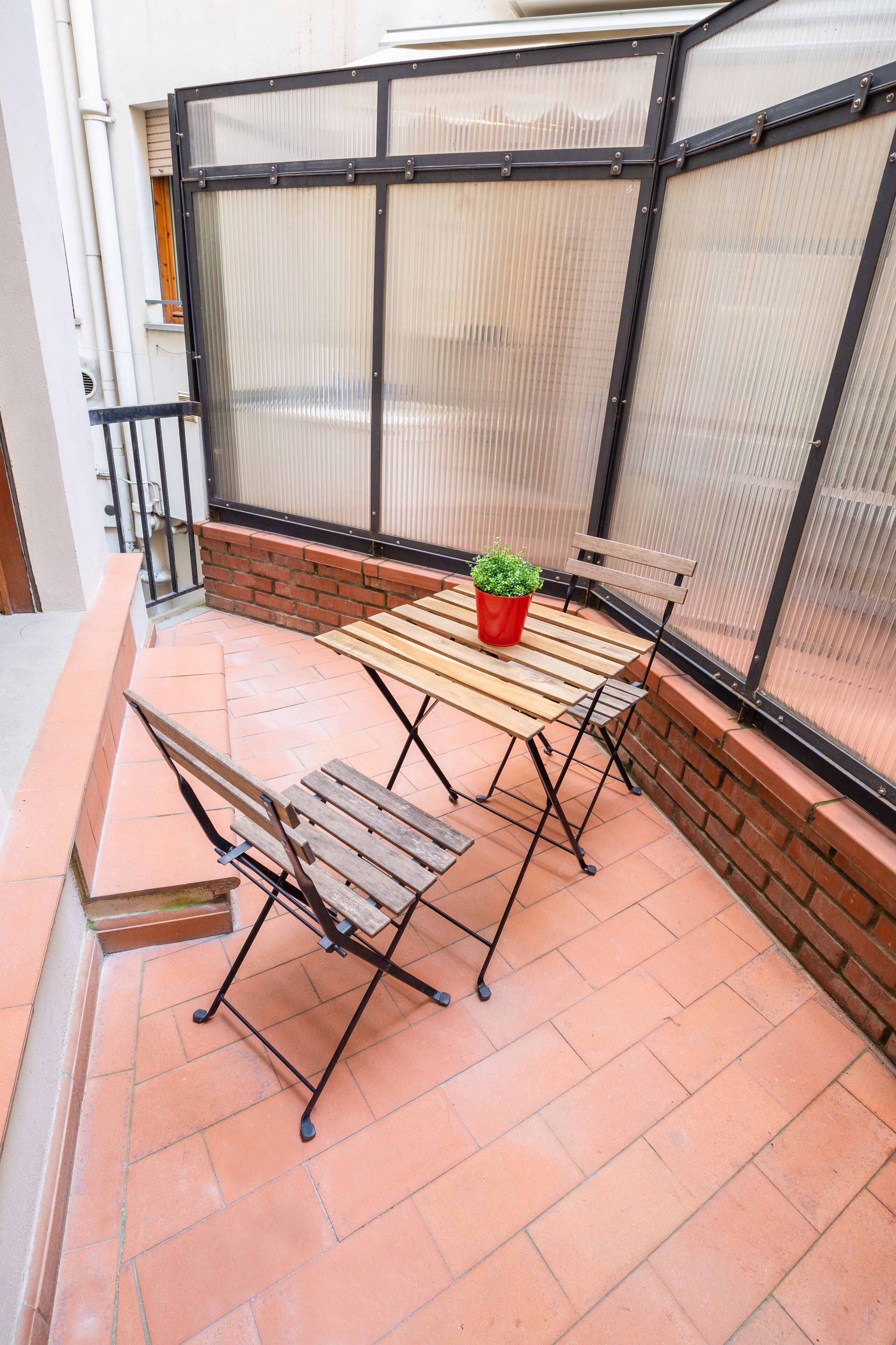 A patio with a wooden table and chairs, a potted plant, and a brick wall.