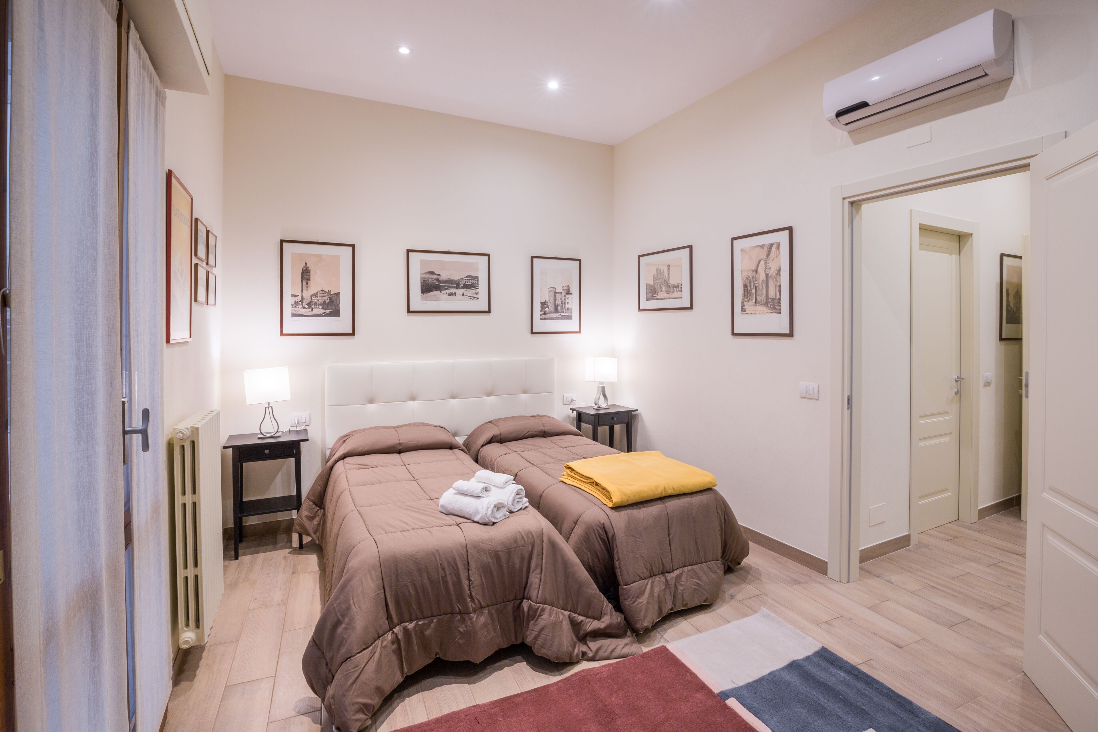 Un dormitorio con dos camas, un radiador, mesitas de noche con lámparas y cuadros en la pared.
