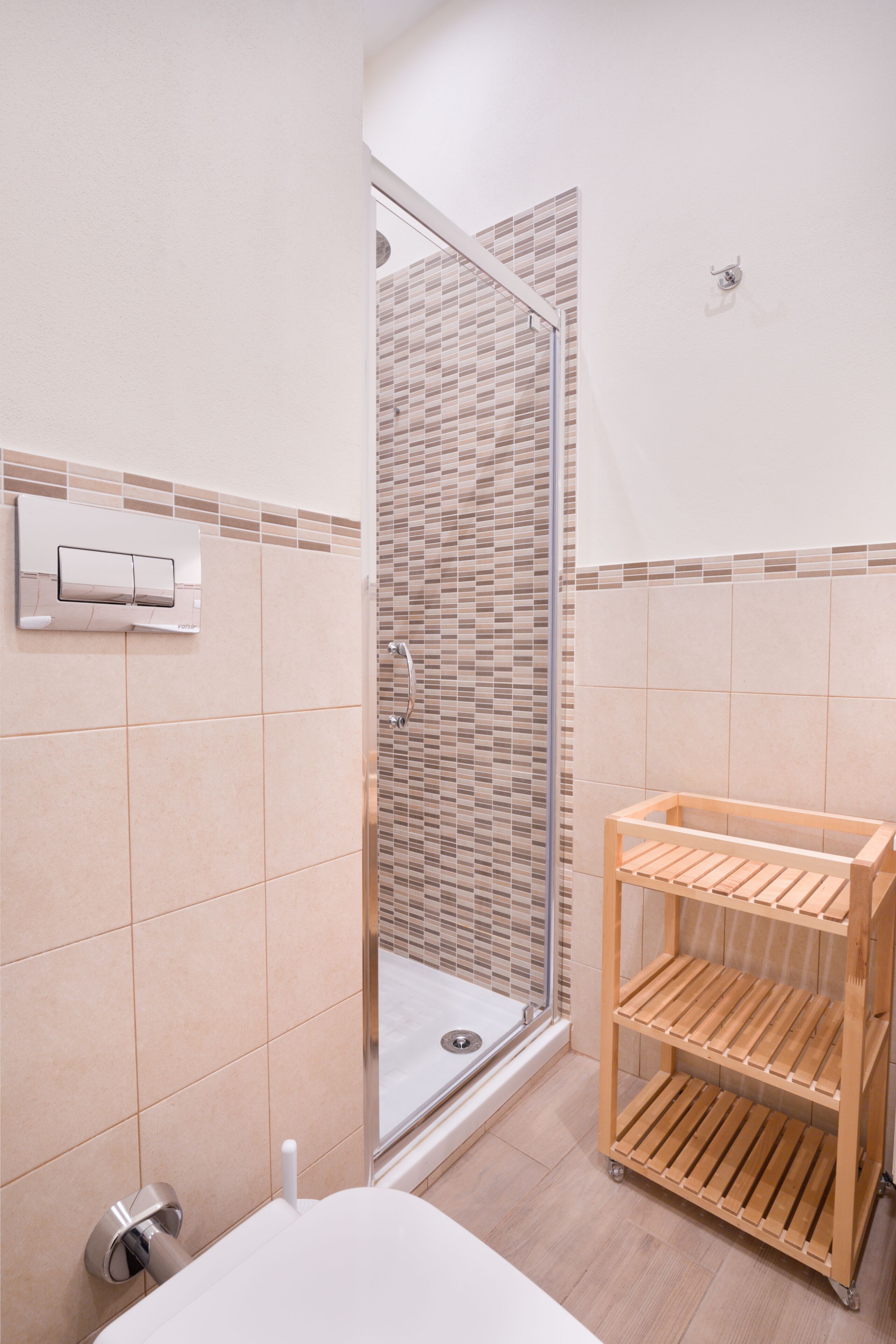 Ein Badezimmer mit Dusche, Toilette und einem Holzregal.