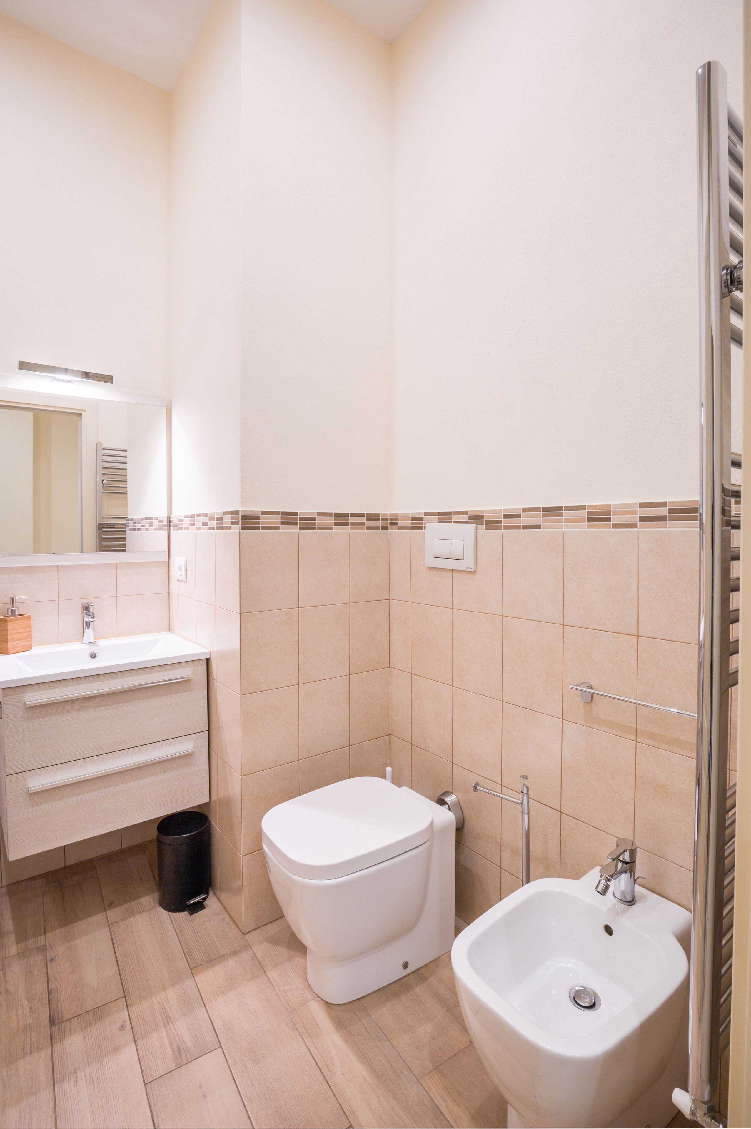 A bathroom with a white sink, toilet, and bidet, a mirror, and a trash can.
