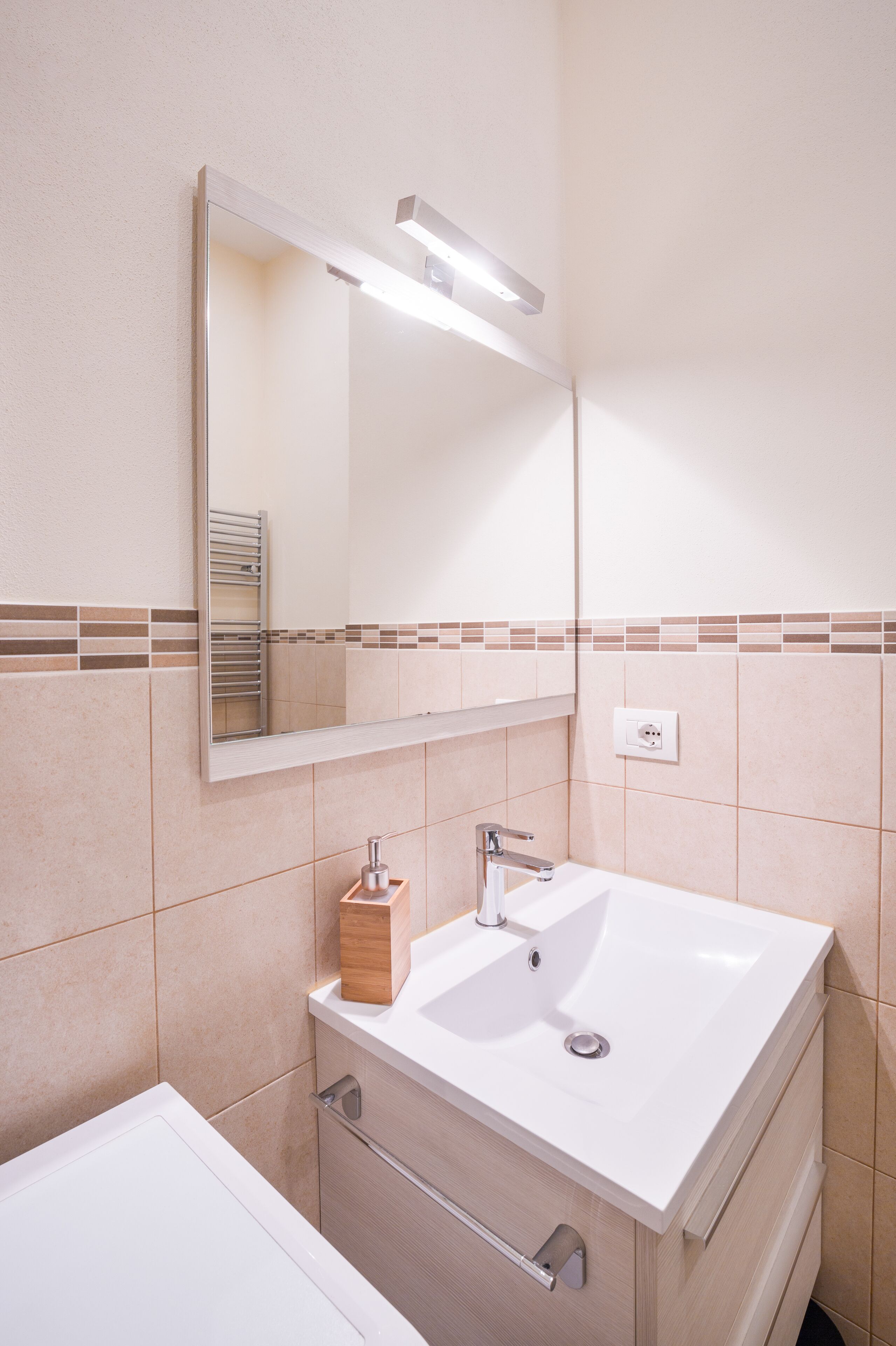 A modern bathroom with a white sink, mirror, and a light fixture above the mirror.