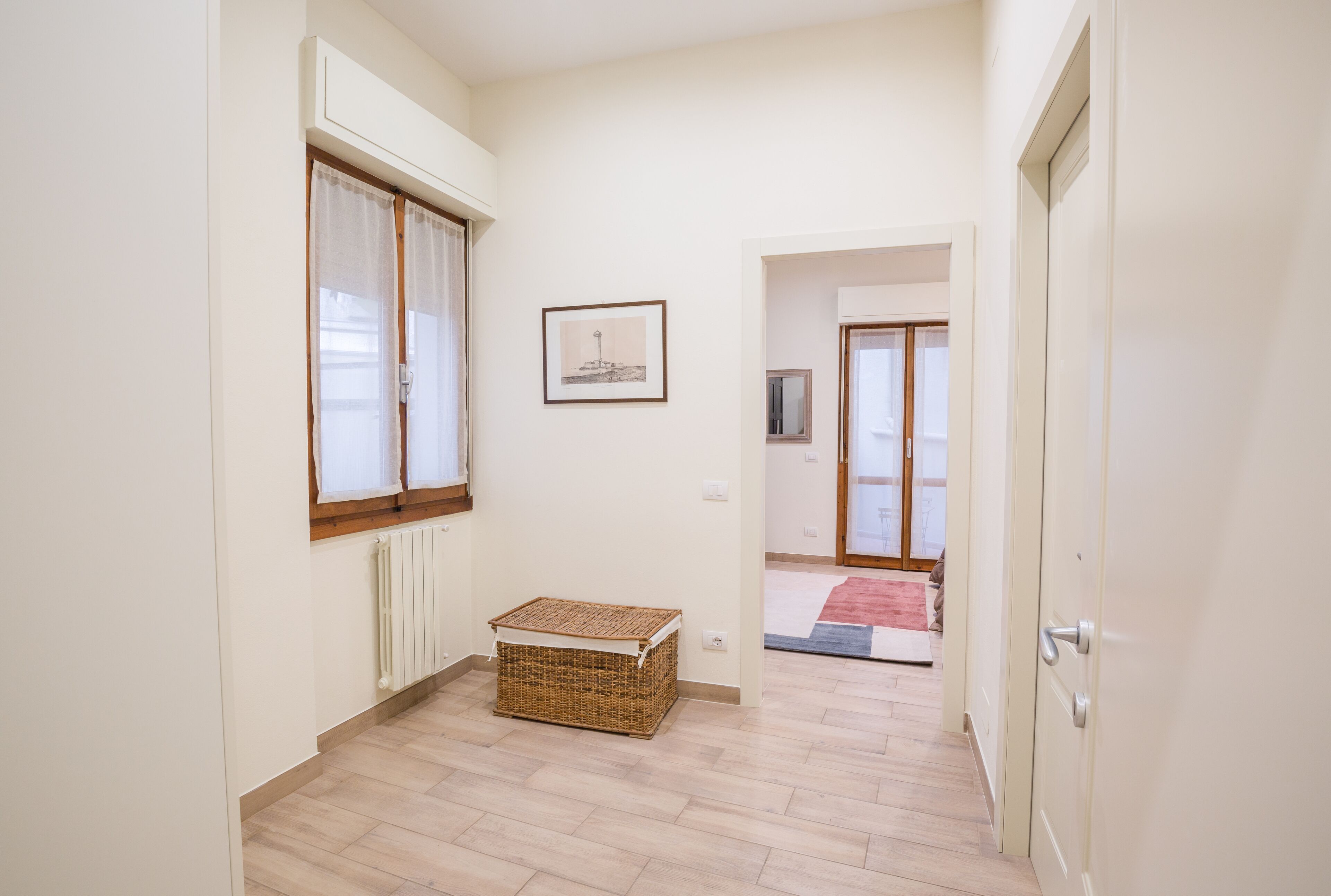 Un pasillo con una cesta de mimbre, un cuadro en la pared y una puerta que da a otra habitación.