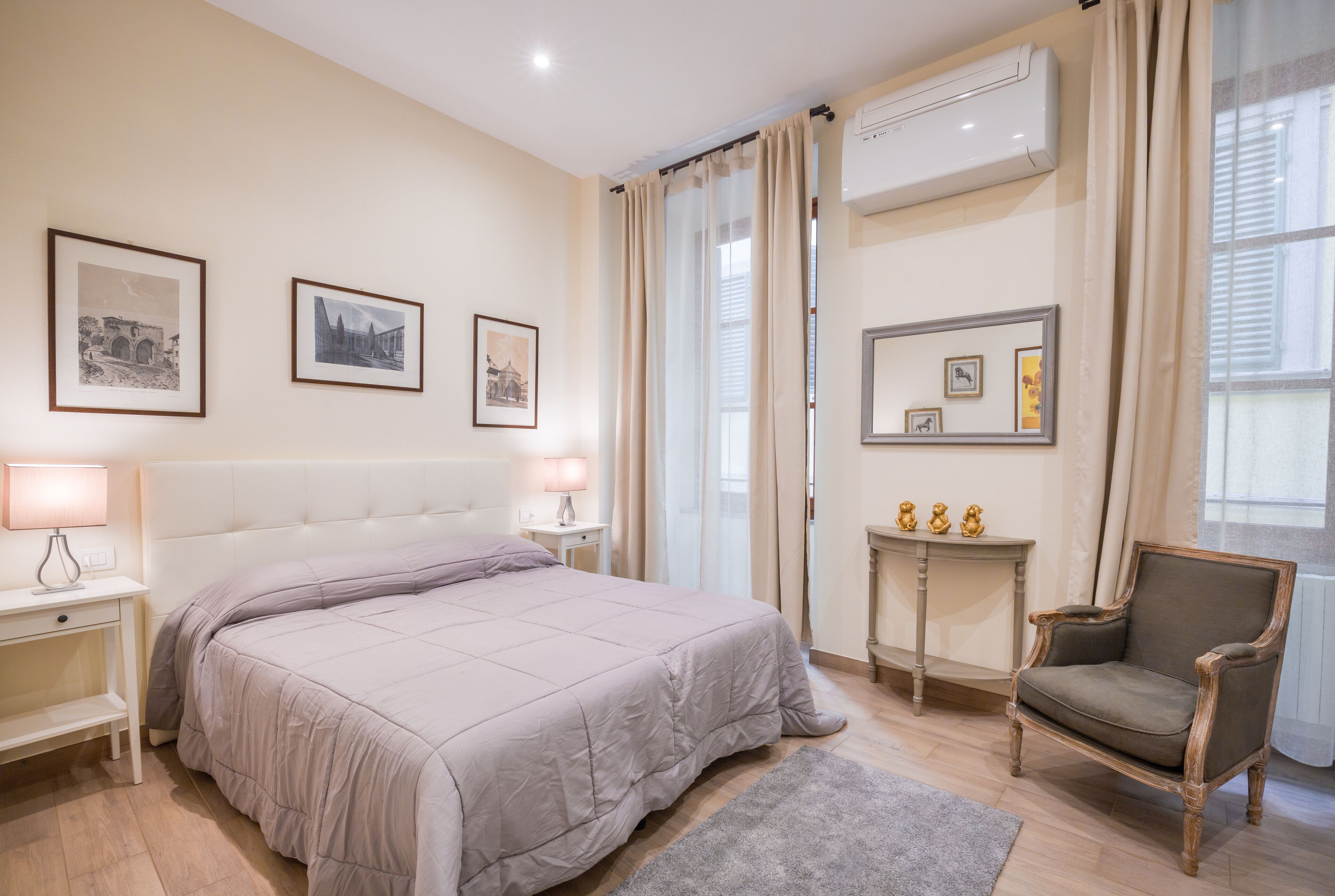 A bedroom with a bed, bedside lamps, a chair, a small table, and framed pictures on the wall.