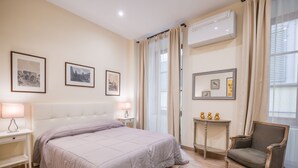 Une chambre à coucher avec un lit, des lampes de chevet, une chaise, une petite table et des tableaux encadrés au mur.