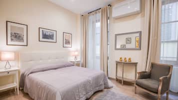 A bedroom with a bed, bedside lamps, a chair, a small table, and framed pictures on the wall.