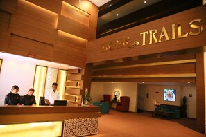 A reception area with a wooden reception desk, a sign reading "TRAILS", and a seating area with chairs and a television screen displaying a tiger. - Tiger Trails Thekkady (Peermade)