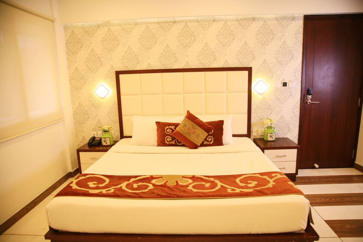 A neatly made bed with a headboard, two bedside tables with lamps, and a wooden door.
