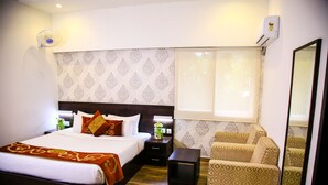 A hotel room with a bed, bedside tables, a chair, a mirror, and a window with curtains. - Tiger Trails Thekkady (Peermade)