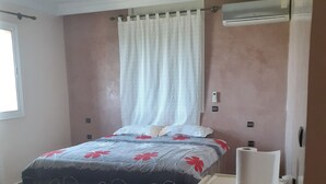 Un dormitorio con una cama, una mesita, un ventanal y un equipo de aire acondicionado.