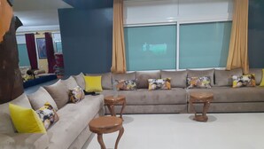 Una sala de estar con un sofá, dos mesitas de madera y un ventanal con cortinas.