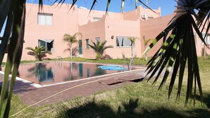 Un edificio moderno con piscina, palmeras y cielo azul despejado.