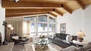 A cozy living room with a high wooden ceiling, a large window with a view of snow-covered trees, a glass coffee table, and a grey sofa with patterned cushions. - Ski-In/Ski-Out Snowmass Estate with Hot Tub, Fireplaces & Expansive Mountain Views (Snowmass Village)