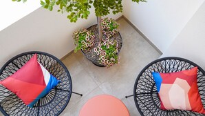 A small patio area with two black wire chairs, each with a red and blue pillow, and a round table. A potted plant with pink flowers is in the center. - The Pearl of Bari (Bari)