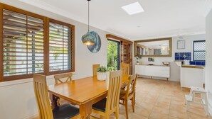 A dining area with a wooden table and chairs, a hanging pendant light, and a view of the garden through the window. - Villa Paralia - Mediterranean Entertainers' Home in The Heart of Currumbin - Min. 3 Night Stays - (Currumbin)