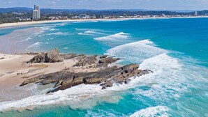 A coastal beach with clear turquoise waters, rocky outcrops, and a distant cityscape. - Villa Paralia - Mediterranean Entertainers' Home in The Heart of Currumbin - Min. 3 Night Stays - (Currumbin)