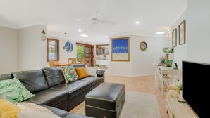 A modern living room with a leather sofa, a flat-screen TV, and a dining area with wooden furniture. - Villa Paralia - Mediterranean Entertainers' Home in The Heart of Currumbin - Min. 3 Night Stays - (Currumbin)