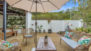 Une terrasse extérieure avec des meubles en osier, une table et une plante suspendue.