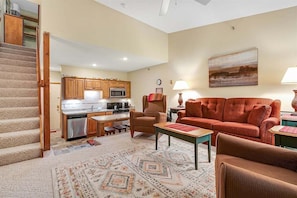 A living room with a sofa, armchair, coffee table, and a painting on the wall. - Sunrise C-108 - Sunday River Condo (Newry)