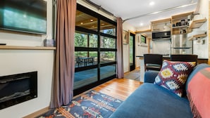 A modern living room with a large TV, a fireplace, and a sofa with a colorful throw. - Two Pines - Unique container home w/hot tub - Downtown - Trailer Parking - Pet friendly (McCall)