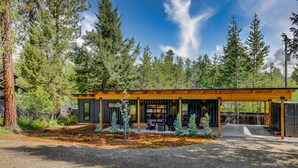 A modern cabin with a covered patio, surrounded by tall trees. - Two Pines - Unique container home w/hot tub - Downtown - Trailer Parking - Pet friendly (McCall)