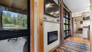 A modern RV interior with a large TV, a fireplace, and a view of the outdoors. - Two Pines - Unique container home w/hot tub - Downtown - Trailer Parking - Pet friendly (McCall)