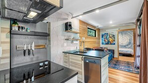 A compact kitchen with a dishwasher, a coffee maker, and a sink. There is a wooden shelf with kitchen utensils and a window above the sink. - Two Pines - Unique container home w/hot tub - Downtown - Trailer Parking - Pet friendly (McCall)