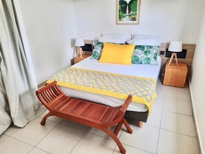 Ein ordentlich eingerichtetes Schlafzimmer mit Bett, Nachttischen, einer Holzbank und einem an der Wand hängenden Kunstwerk.