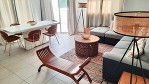 A modern living room with a dining area, a sofa, a coffee table, and a floor lamp. - Superbe Appartement à Saint François Direct sur la Plage (Saint François)