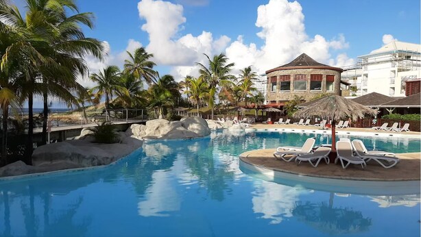 A resort pool with lounge chairs and palm trees. - Superbe Appartement à Saint François Direct sur la Plage (Saint François)