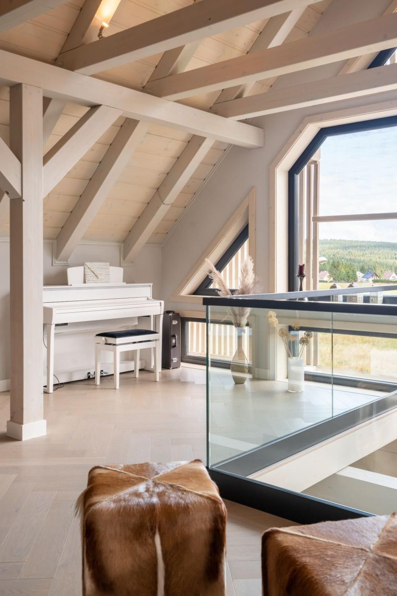 A spacious room with a sloped ceiling, a piano, a glass table with a vase, and a view of a forested area.