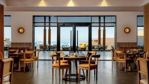 Une salle à manger spacieuse, dotée de meubles en bois et de grandes fenêtres offrant une vue sur la mer.