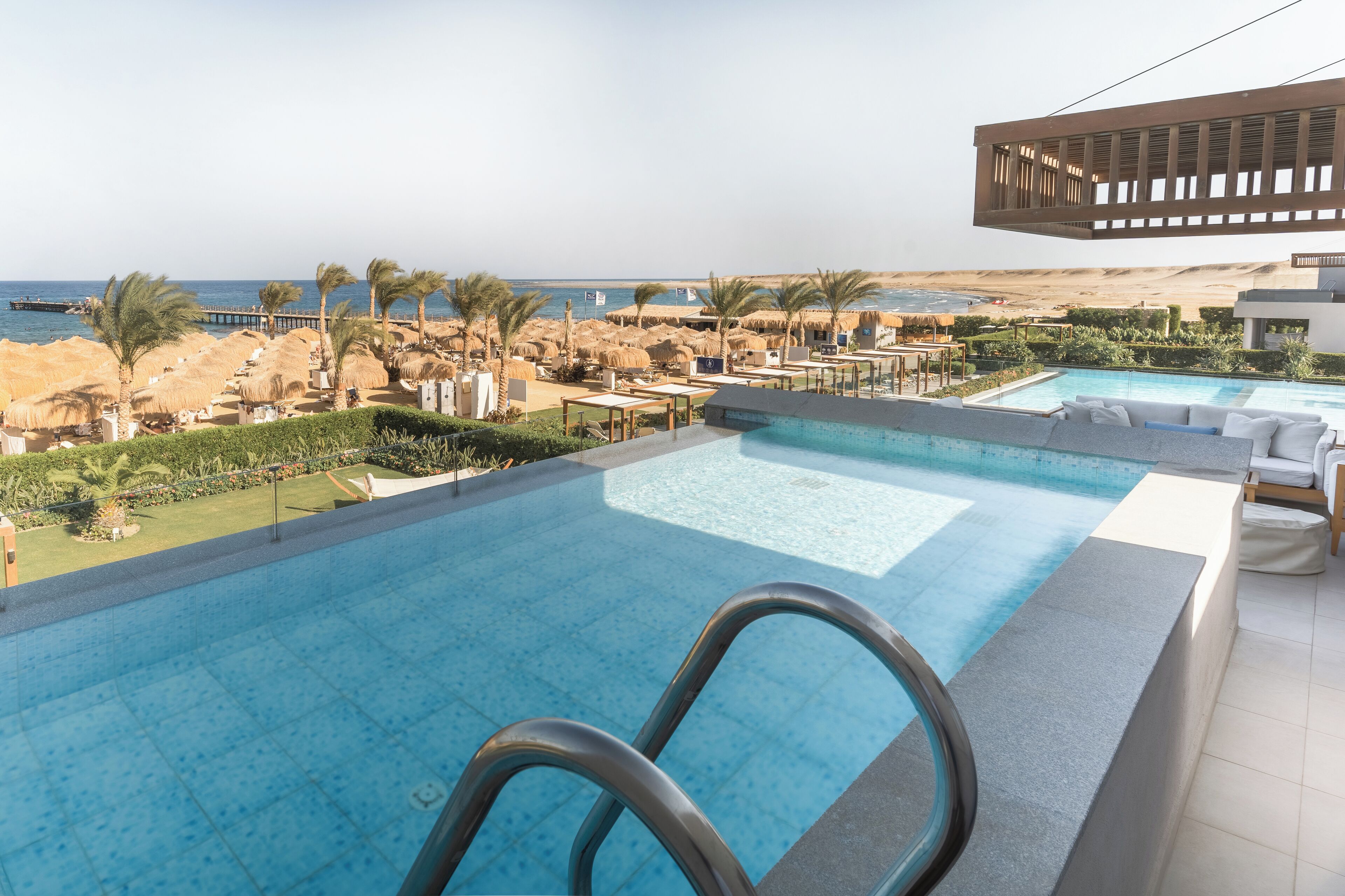 Zona de piscina con vistas al mar, palmeras y una playa.