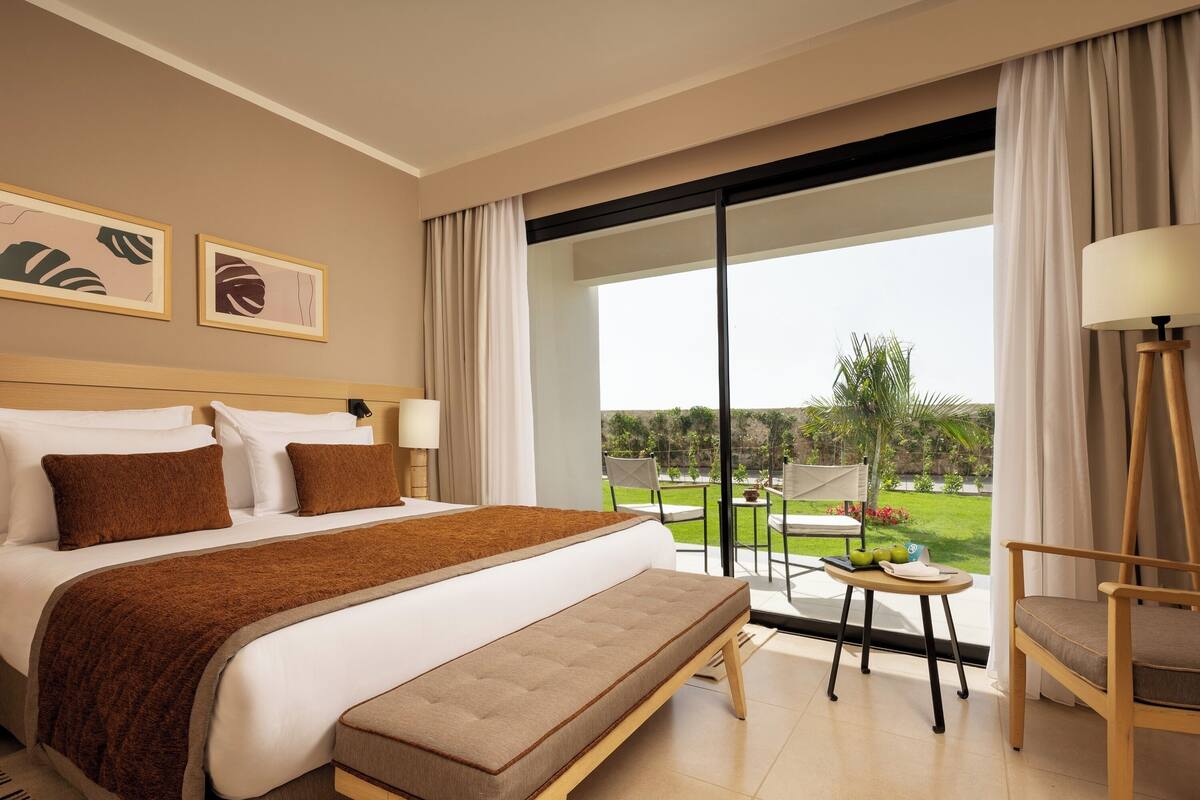 A hotel room with a large bed, a bedside table, a chair, and a view of the outdoors.