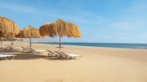 Une plage avec des chaises longues et des parasols en chaume.