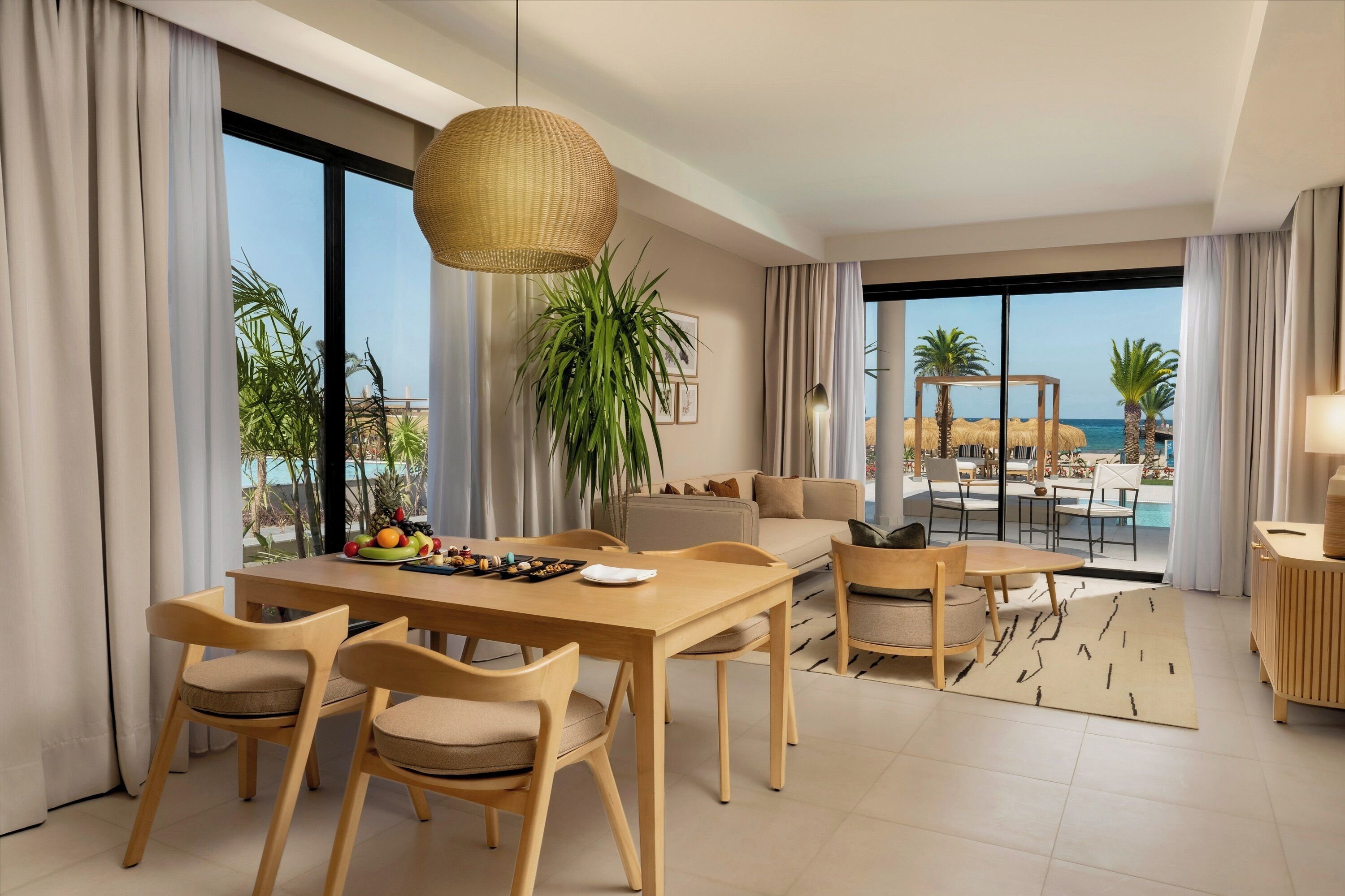 Habitació d'hotel moderna amb zona de dinar, sofà, taula de cafè i vistes a la platja.