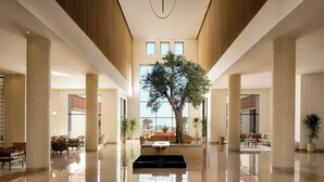 Un hall d’entrée spacieux, agrémenté d’un arbre central, de grandes fenêtres et d’un sol réfléchissant.